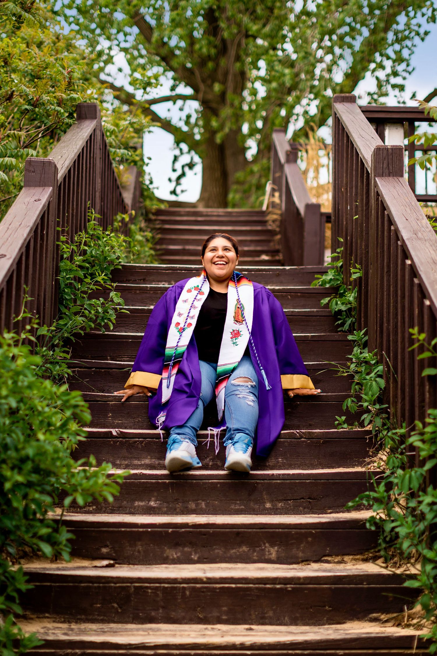 Natural senior portrait of Alejandra sitting casually on sandy stairs with her gown gathered around her.