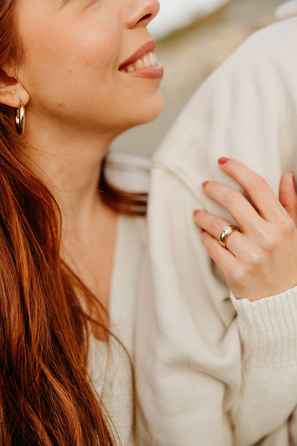 Close up portrait showing a gold ring on hand and auburn hair against a cozy cream sweater background.