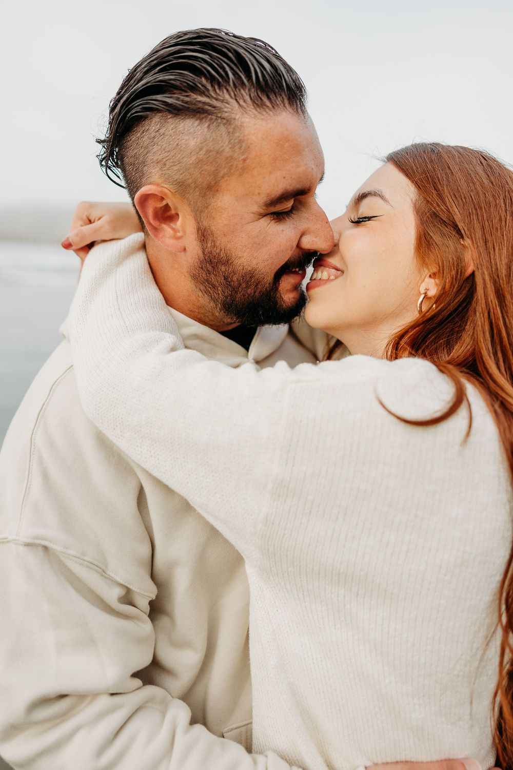 Romantic couple in white sweaters sharing intimate kisses against a light background in a portrait series.