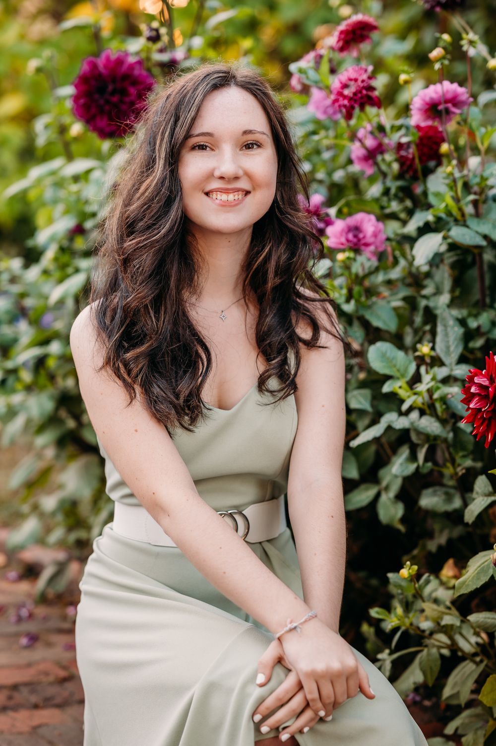 A bright outdoor portrait in a garden with vibrant magenta dahlias, featuring a beige dress against a natural background.