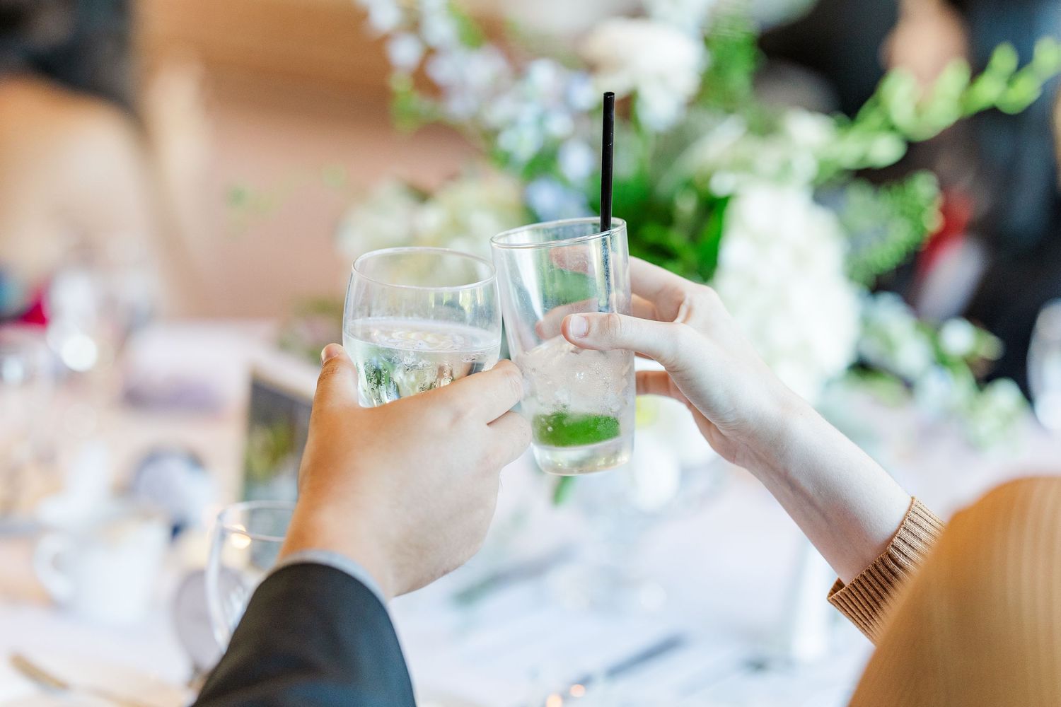 Two hands raise glasses in a celebratory toast with mint garnished cocktails during an elegant event.