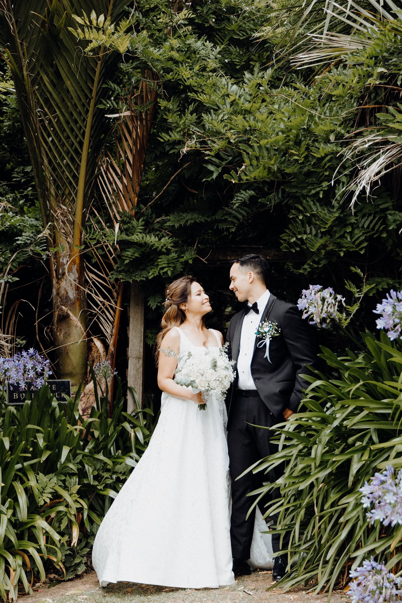 A bride and groom share a joyful moment in a lush tropical garden setting captured by Apertured Media Auckland Wedding Photographer.