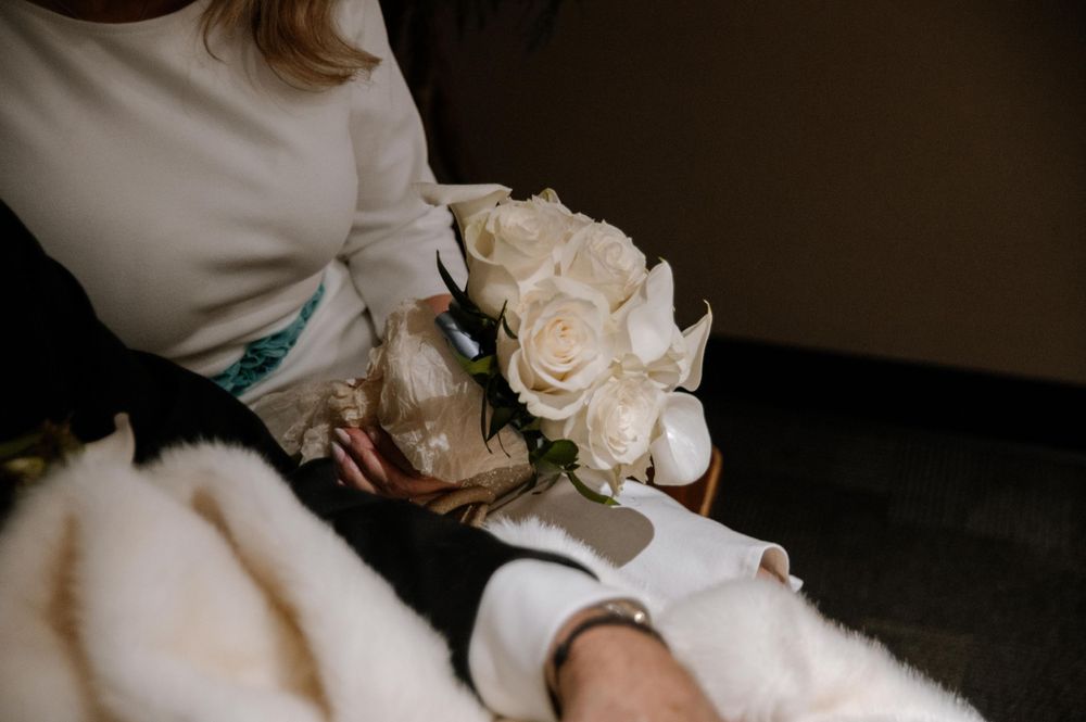Someone holds a delicate bouquet of cream-colored roses against a dark background.