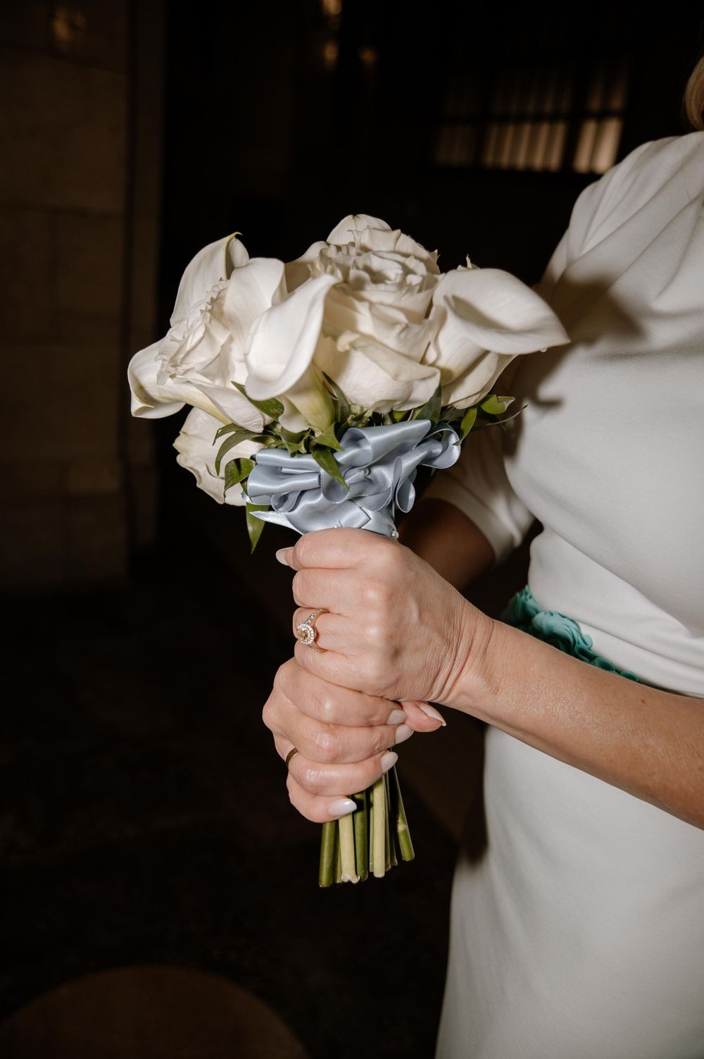 A close-up of a bridal bouquet with white roses held by hands wearing a wedding ring.