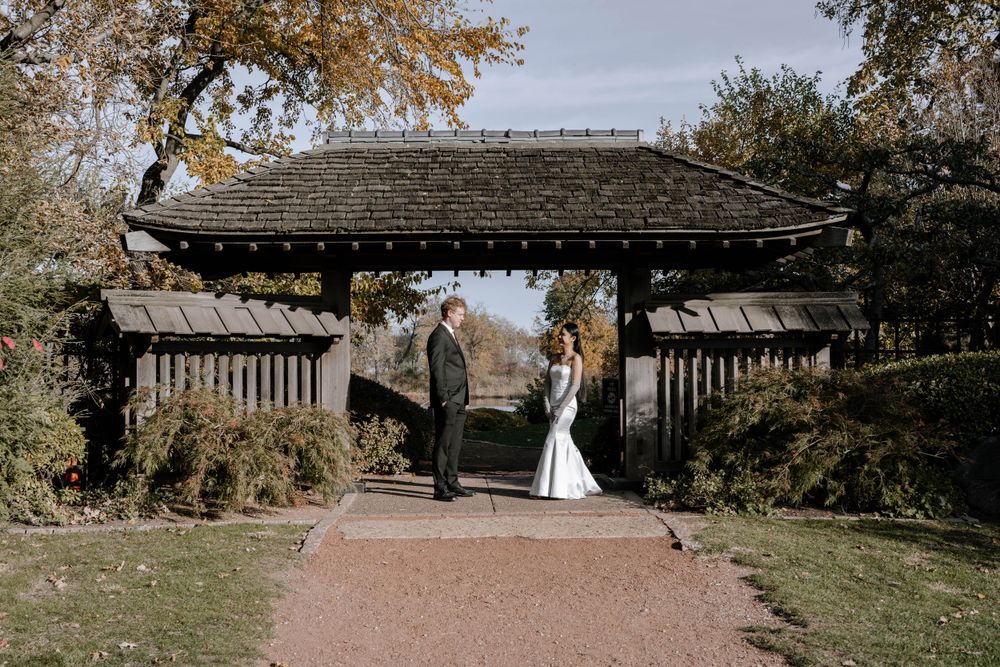 A romantic garden wedding scene beneath an ornate wooden gate structure surrounded by autumn foliage.
