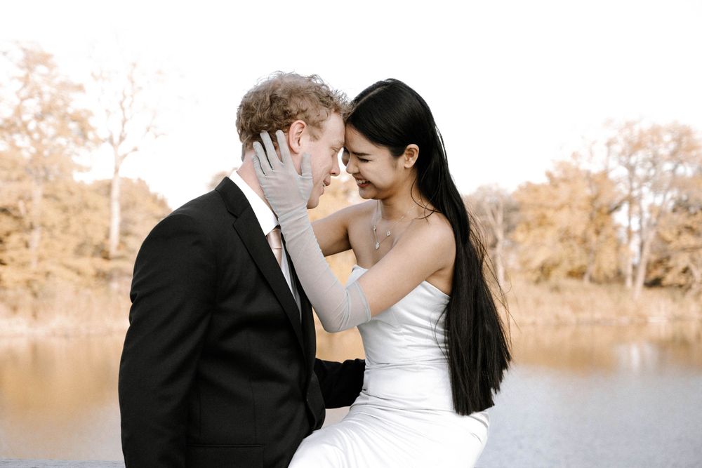 A romantic wedding couple shares a tender moment by a tranquil lake during autumn.
