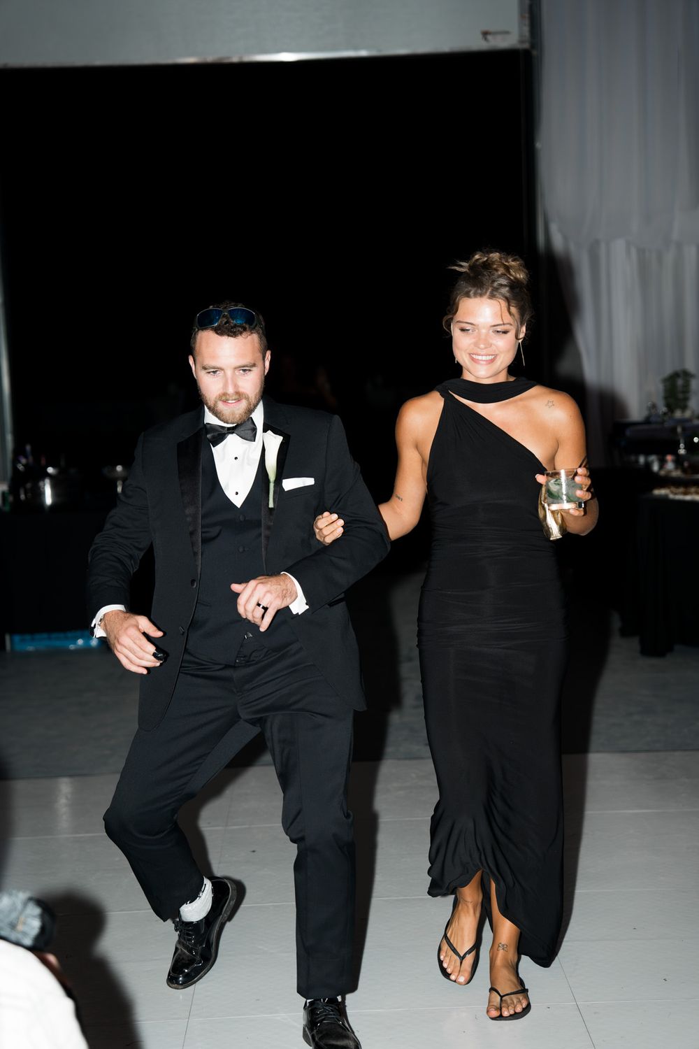 A couple at a formal event dances together, with the woman wearing a black gown and man in a tuxedo.