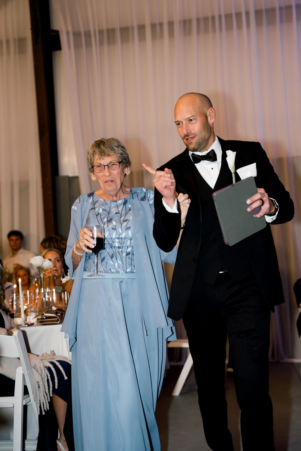 Two attendees at a formal reception give a speech together, with the woman in blue and the man in a tuxedo.
