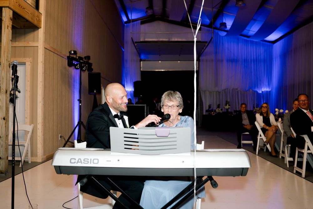 Two people perform music behind a white keyboard setup at an event venue illuminated with blue accent lighting.