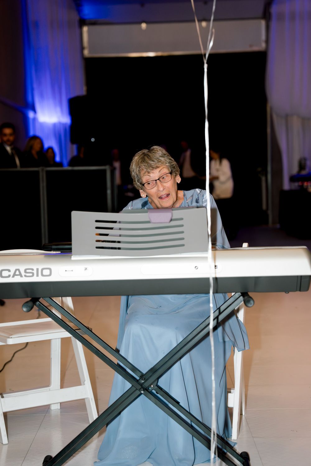 Musician plays a Casio keyboard on a stand during an event with blue lighting in the background.
