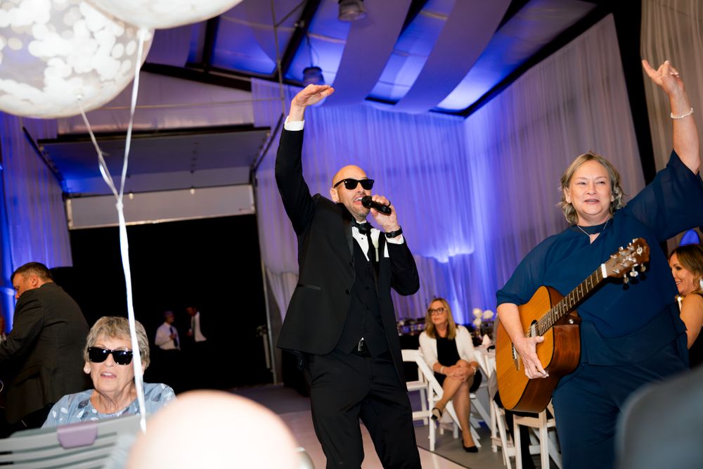 Performers entertain wedding guests with live music and singing under blue stage lighting.