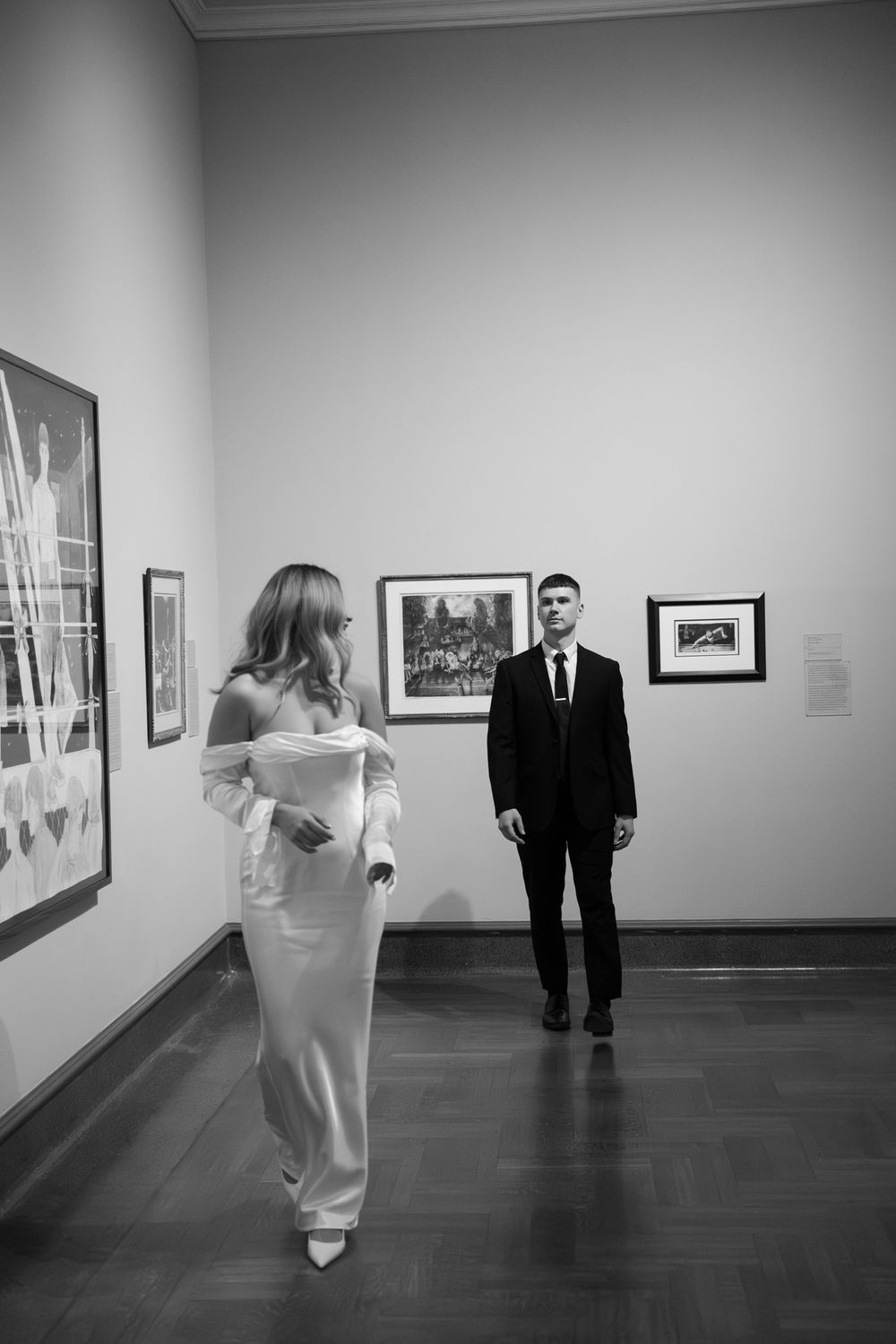 Elegant couple in formal attire poses in an art gallery featuring black and white photographs.