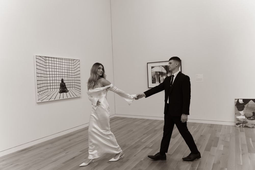 A couple in formal wear dances in a minimalist art gallery space.