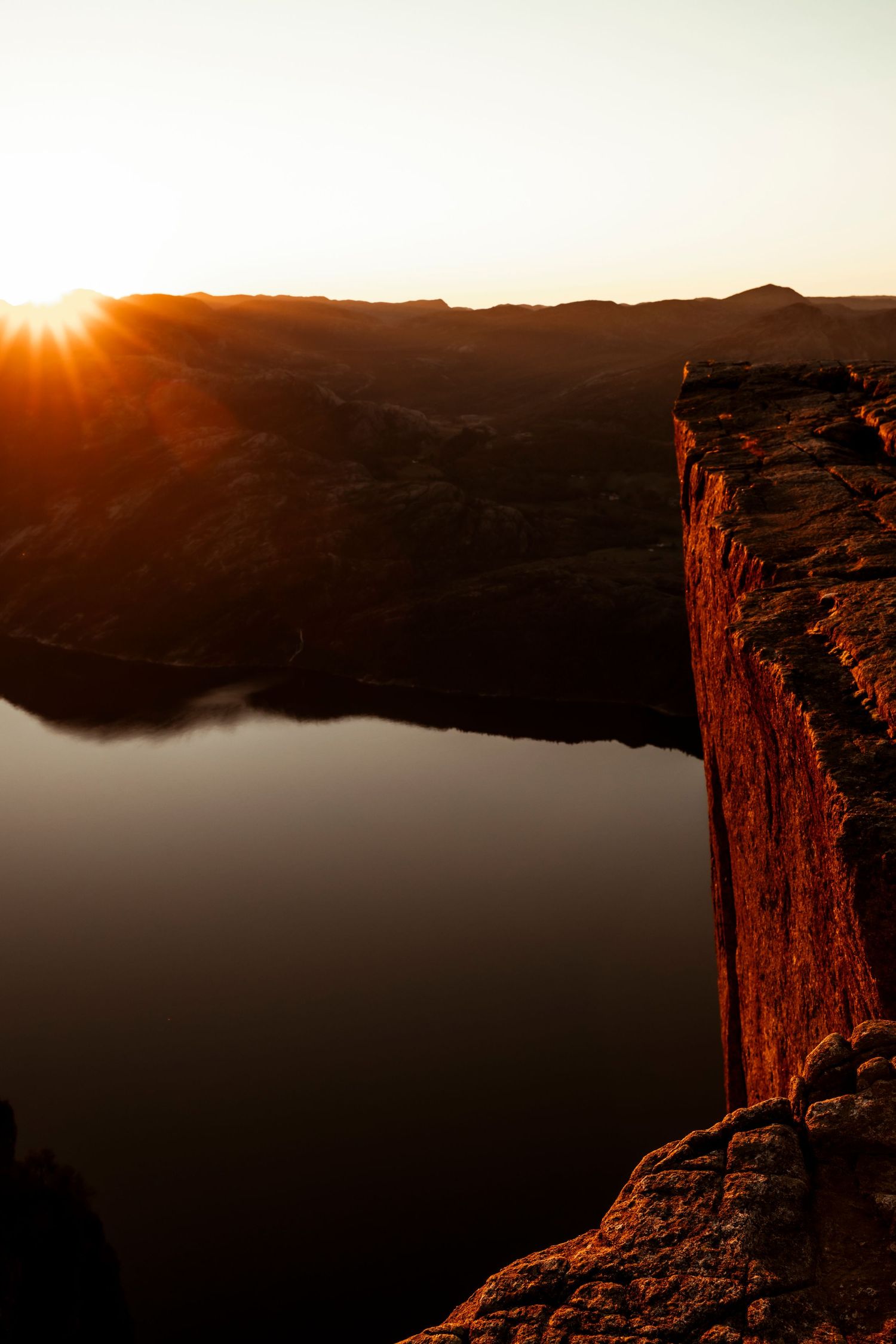 Dramatic sunset illuminates steep red canyon cliffs overlooking a dark valley in a rugged desert landscape.