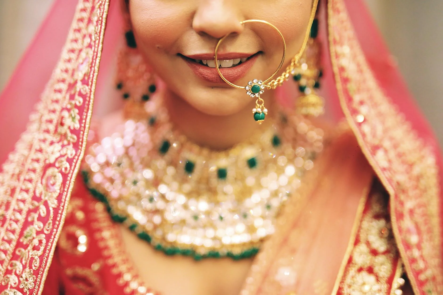 Close-up detail of traditional Indian bridal jewelry featuring ornate gold necklace with emerald stones and nose ring.
