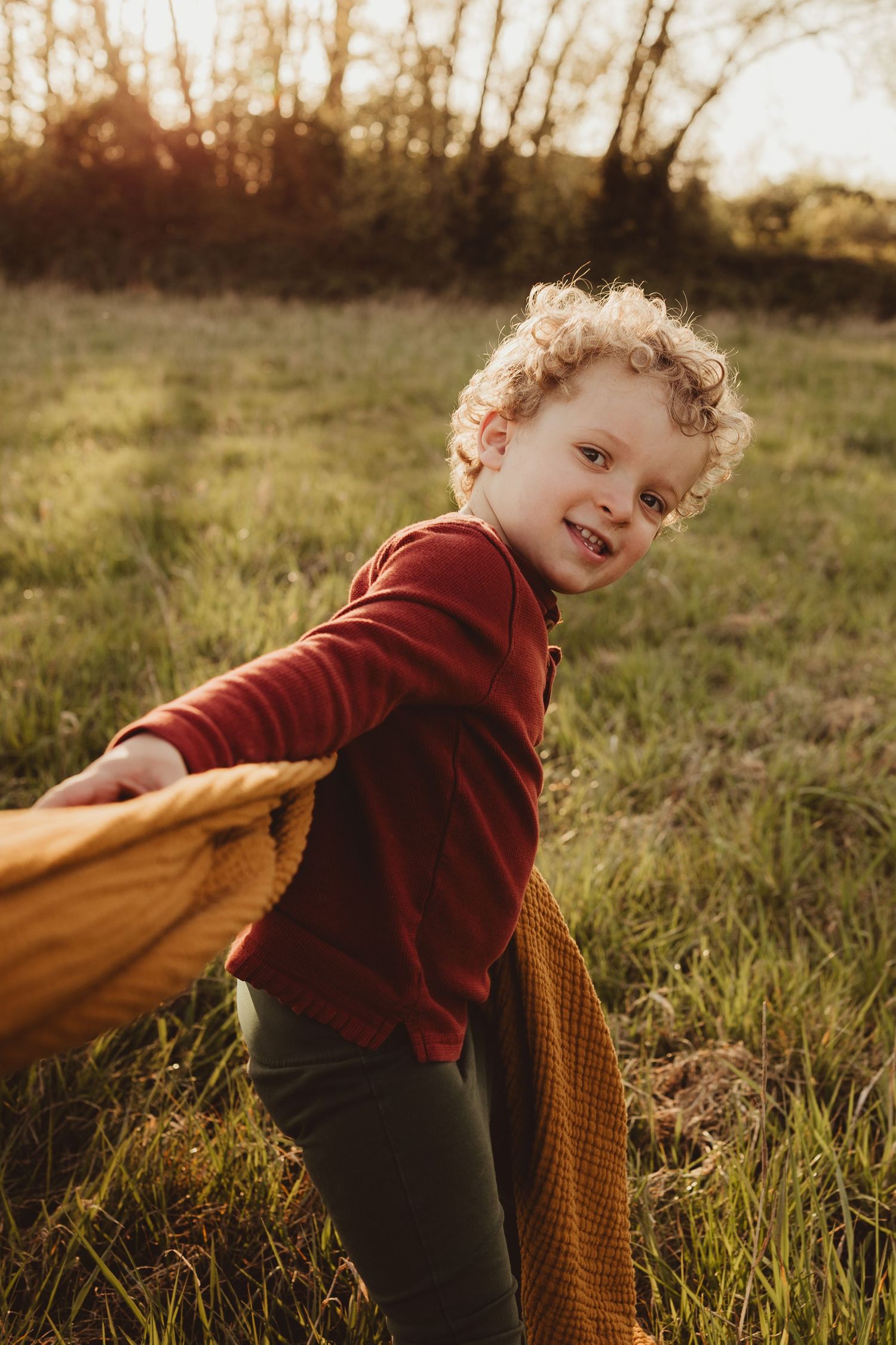 A child in a burgundy sweater plays joyfully in a sun-drenched field at golden hour.