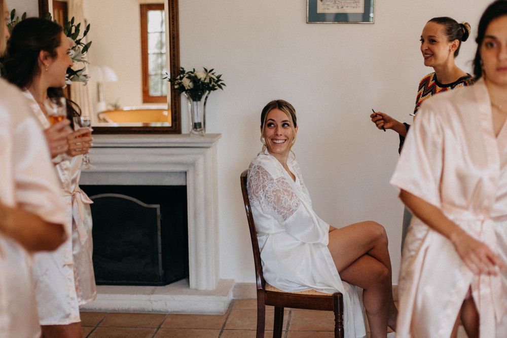 Bridal party members in white robes gather around a fireplace during wedding preparations.