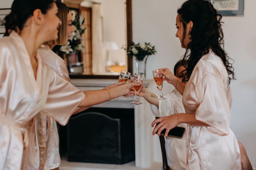 Two people in silk robes toast with champagne glasses during wedding preparation.