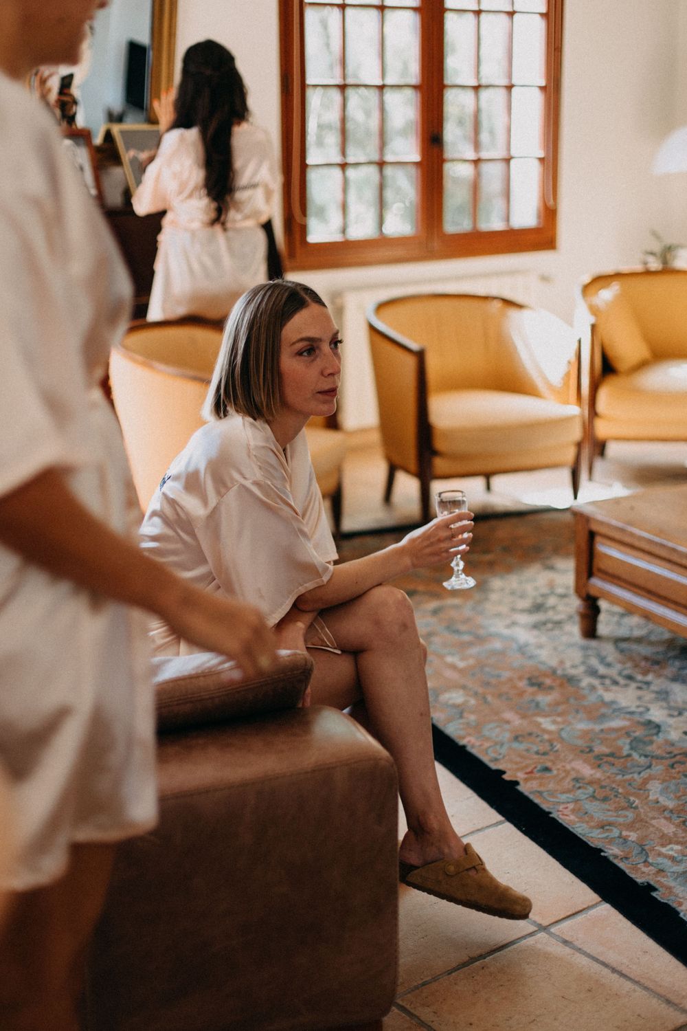 Person in white attire relaxes on a couch holding a drink in an elegant living room setting.