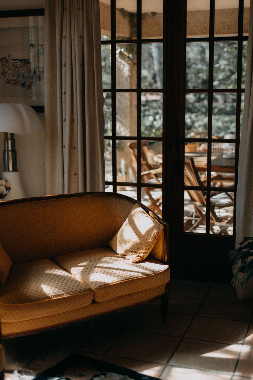 Sunlit cozy living room with vintage couch and French doors casting window shadows.