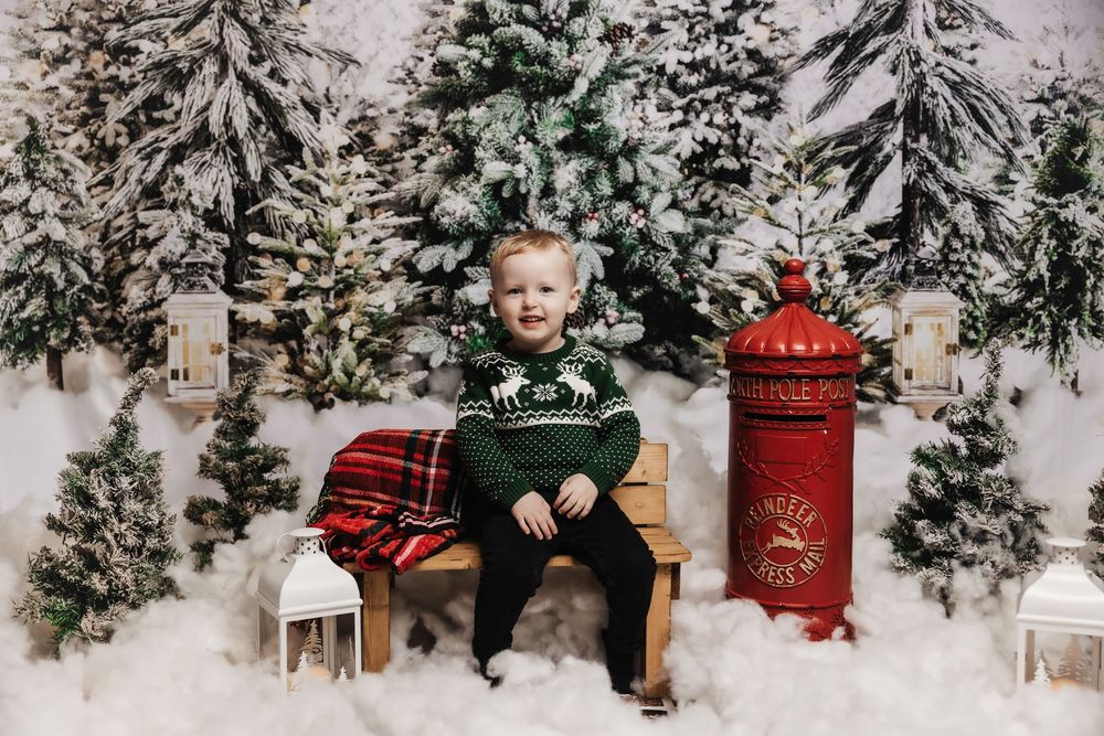 Festive winter scene with snowy evergreens, vintage red mailbox, plaid blanket, and holiday decor in white studio setting.