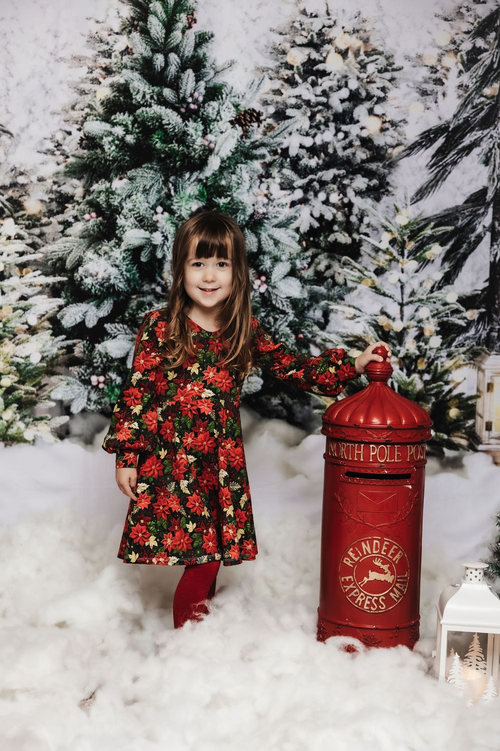 Holiday scene with floral dress, snow-covered Christmas trees and a decorative red express mailbox against white snowy backdrop.