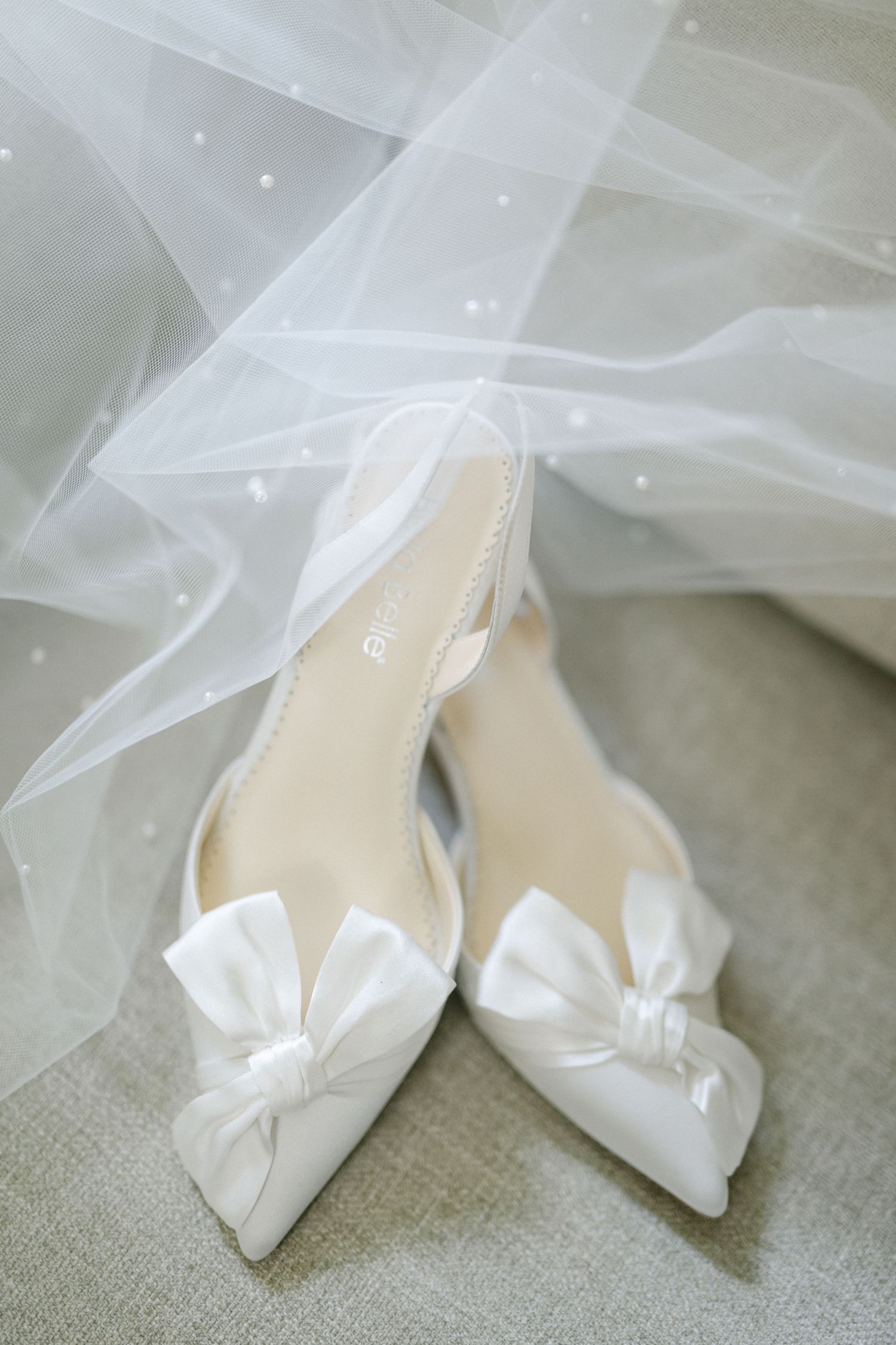 A bride in a classic white strapless gown smiling while holding a bouquet of white flowers and eucalyptus.