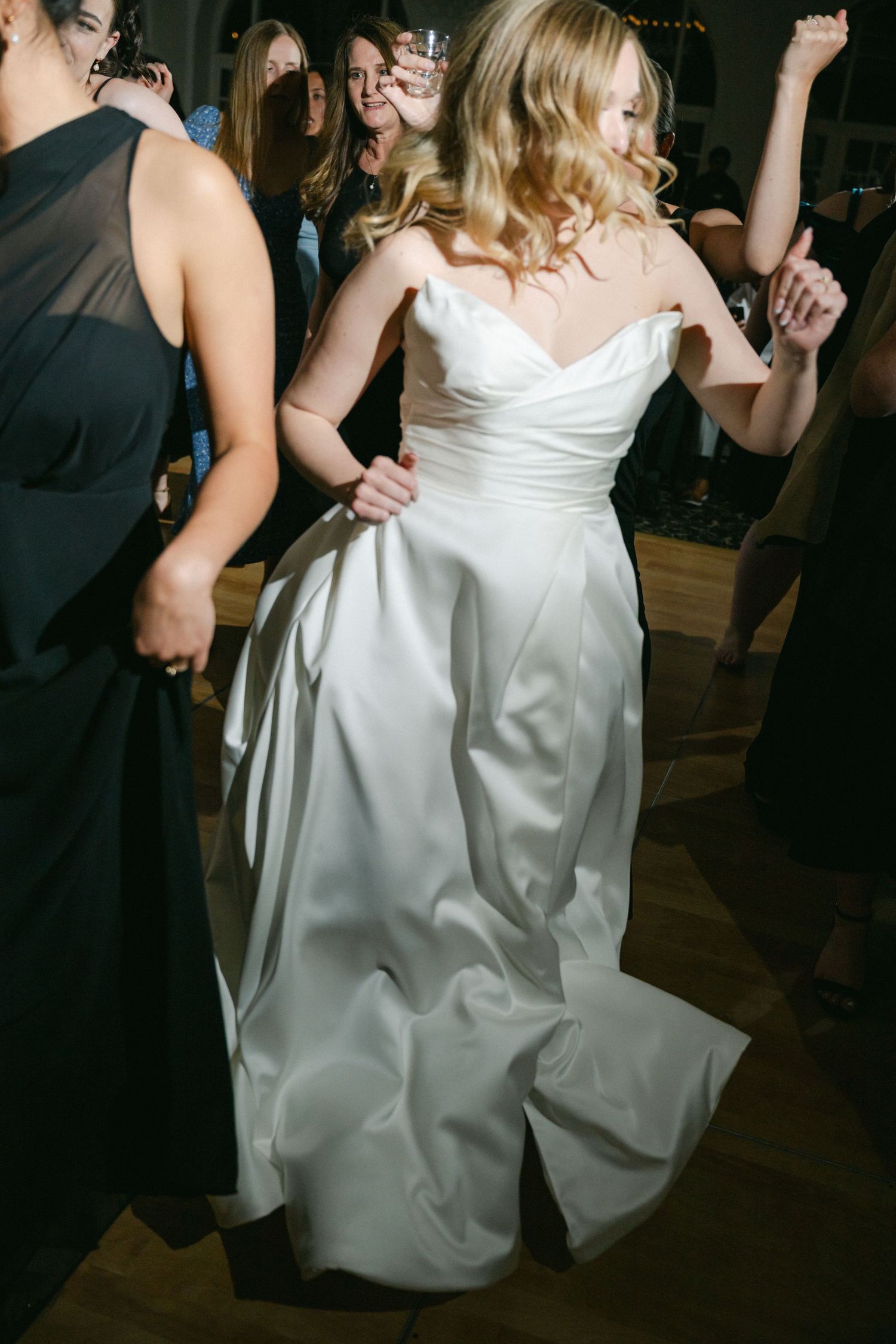 A guest in a navy suit dances at an elegant reception venue with arched windows and decorative lighting.