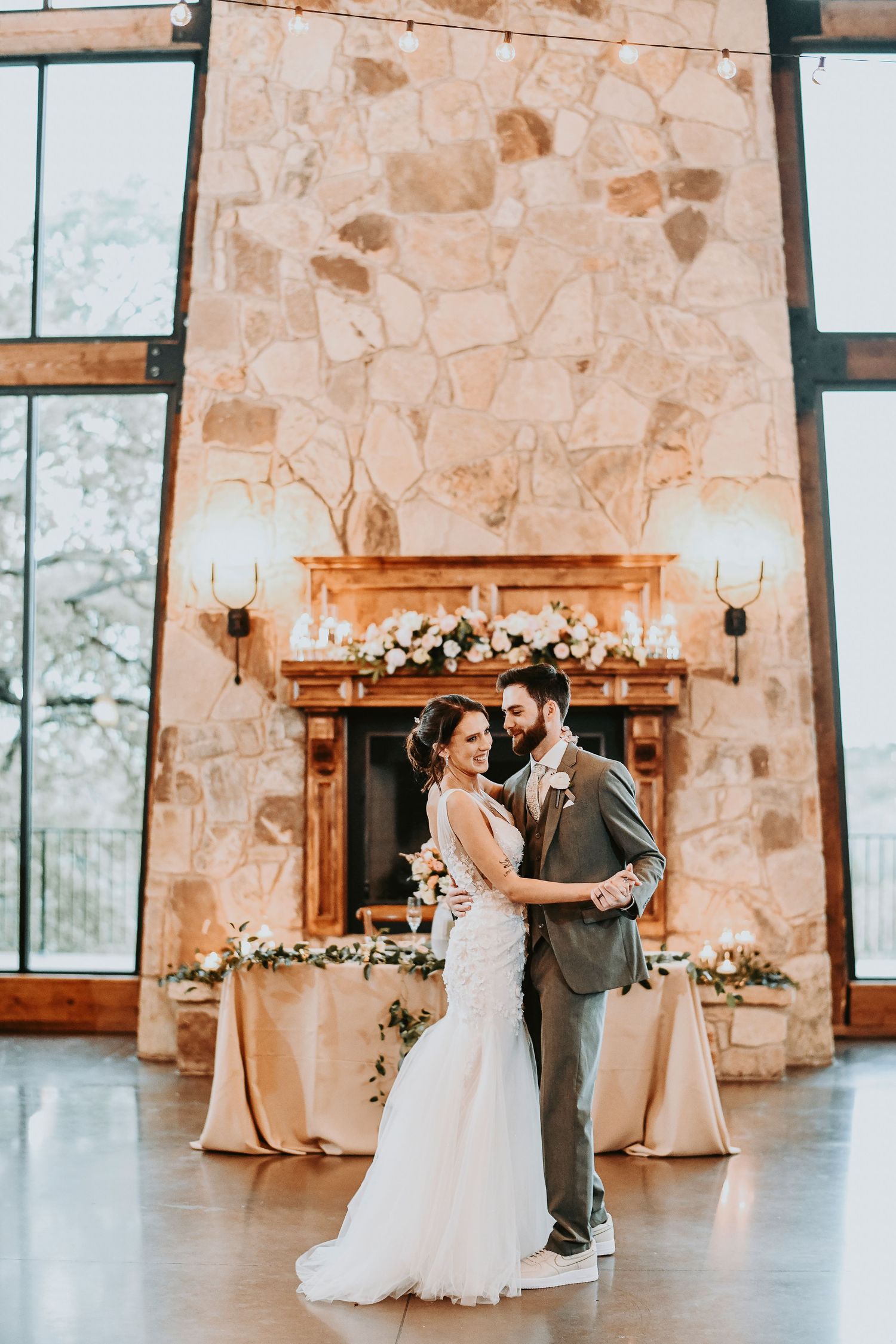 Bride and groom embracing in front of the stone fireplace at The Lodge, decorated with greenery and spring florals for their indoor wedding