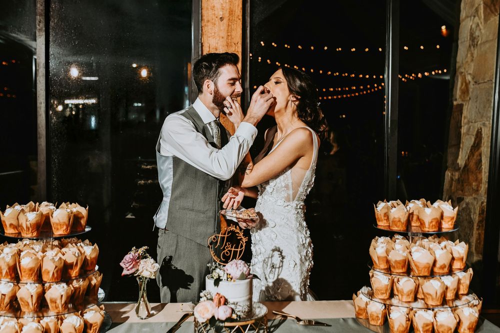 Wedding cake cutting with cupcakes in kraft paper wrappers displayed on tiered towers in the background.
