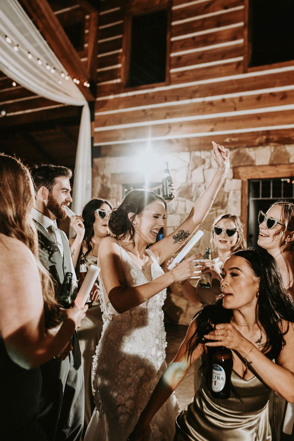 Bridesmaids hyping up the bride as she dances in the center of the crowd under twinkling lights.
