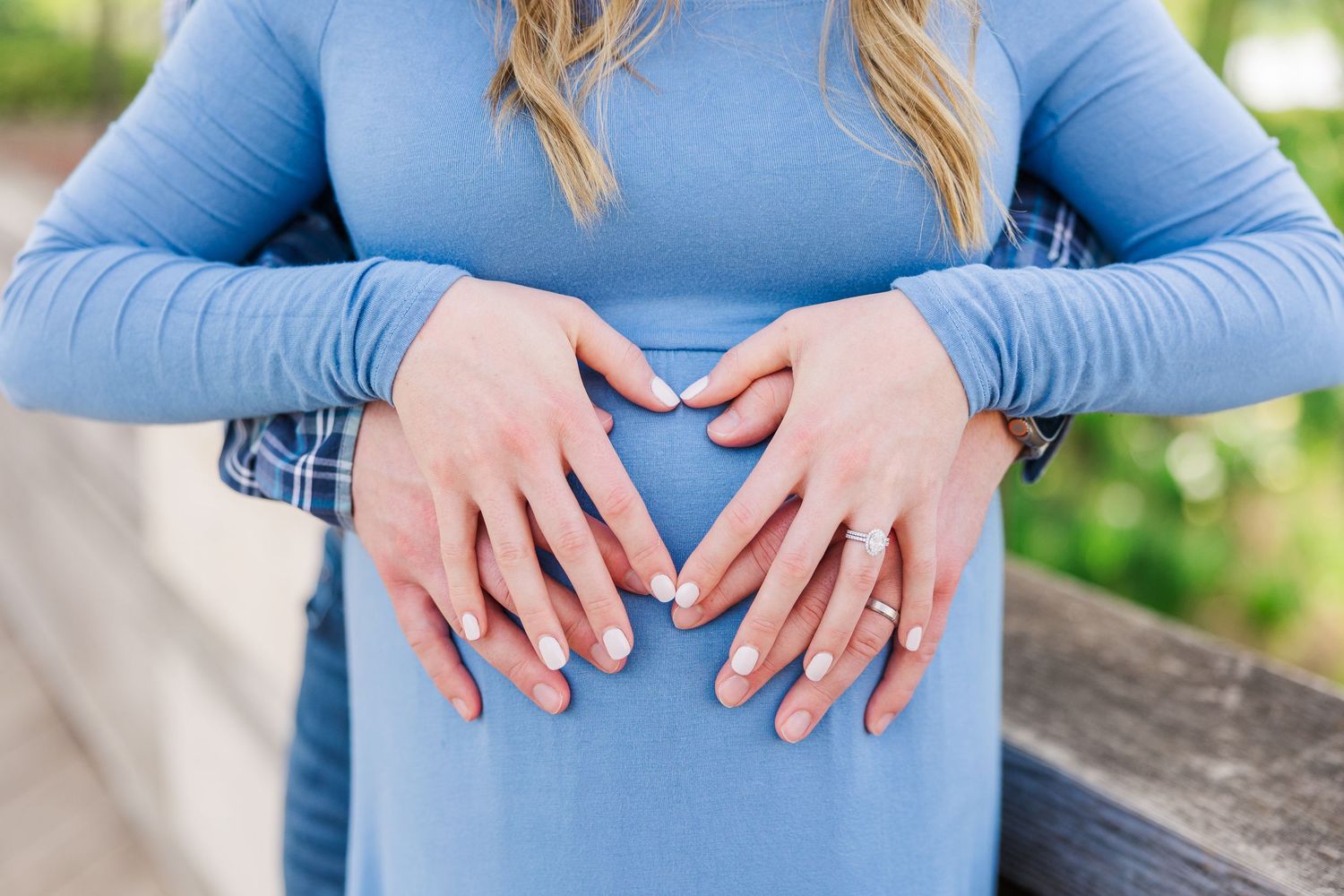 Hands forming a heart shape over blue maternity shirt with blurred green background at Chicago Botanic Garden