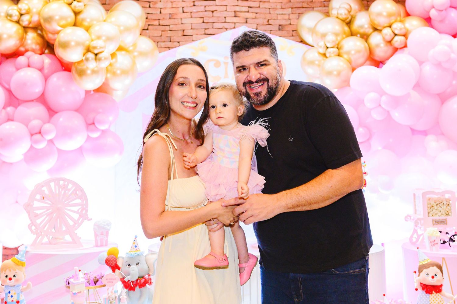 Family celebrates at pink and gold balloon themed birthday party with decorative backdrop for special occasion.