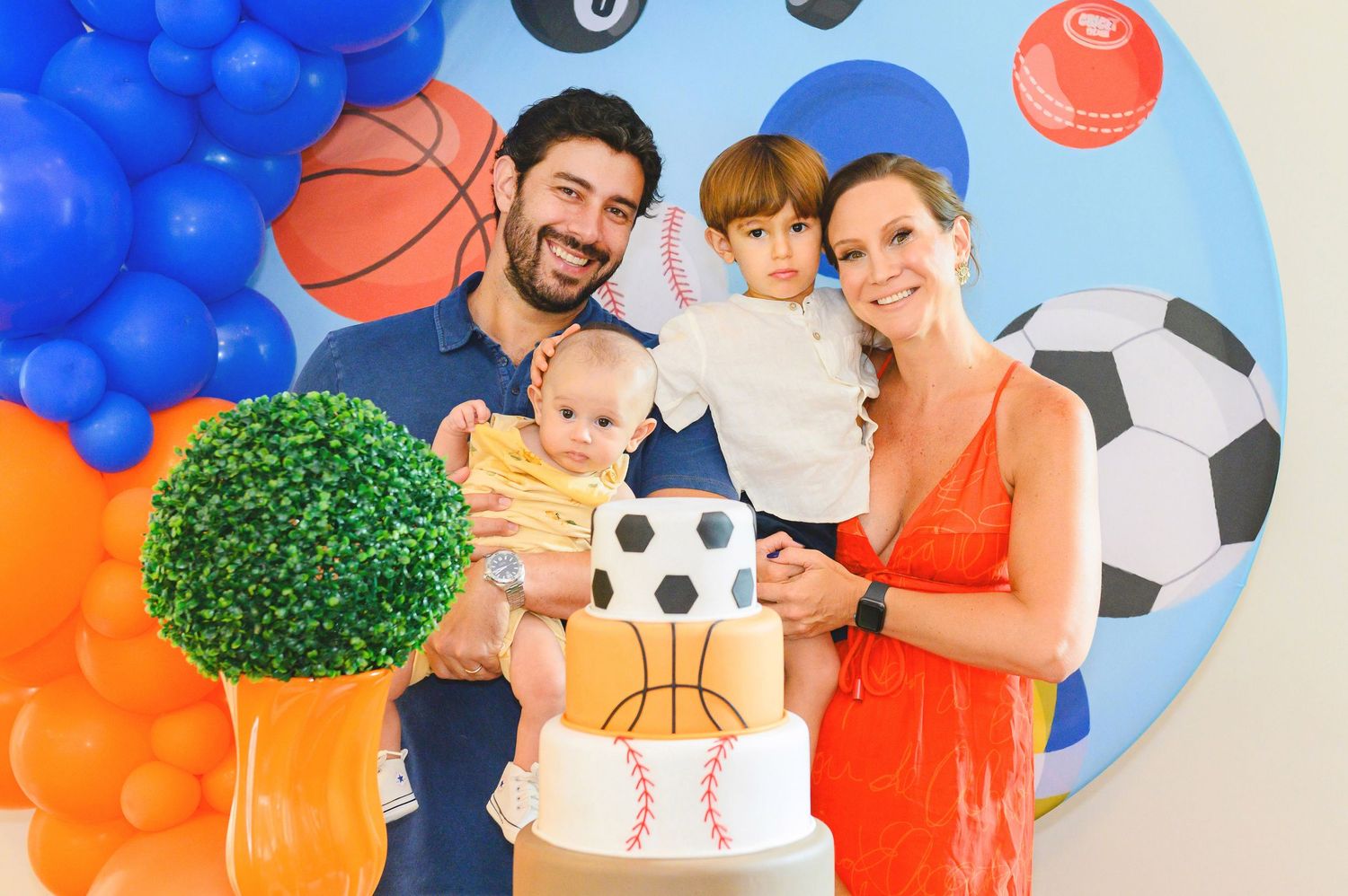 Sports-themed birthday party celebration with balloons, decorative spheres, and cake against blue and white backdrop.