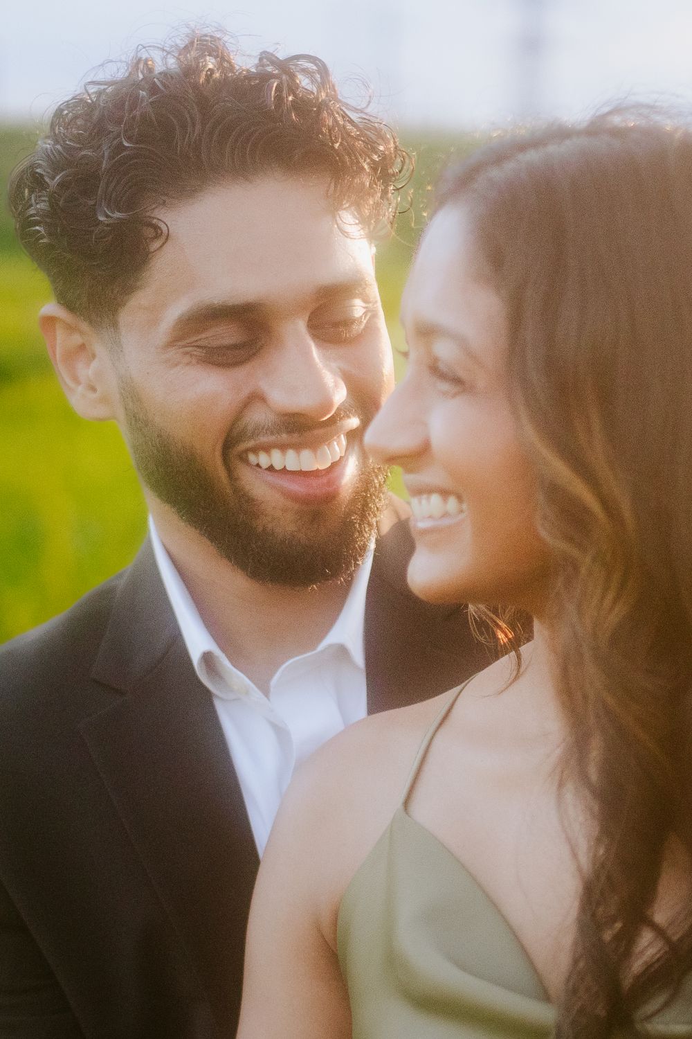 Close up of a tender romantic moment between a couple smiling together in golden sunlight against a blurred outdoor background.