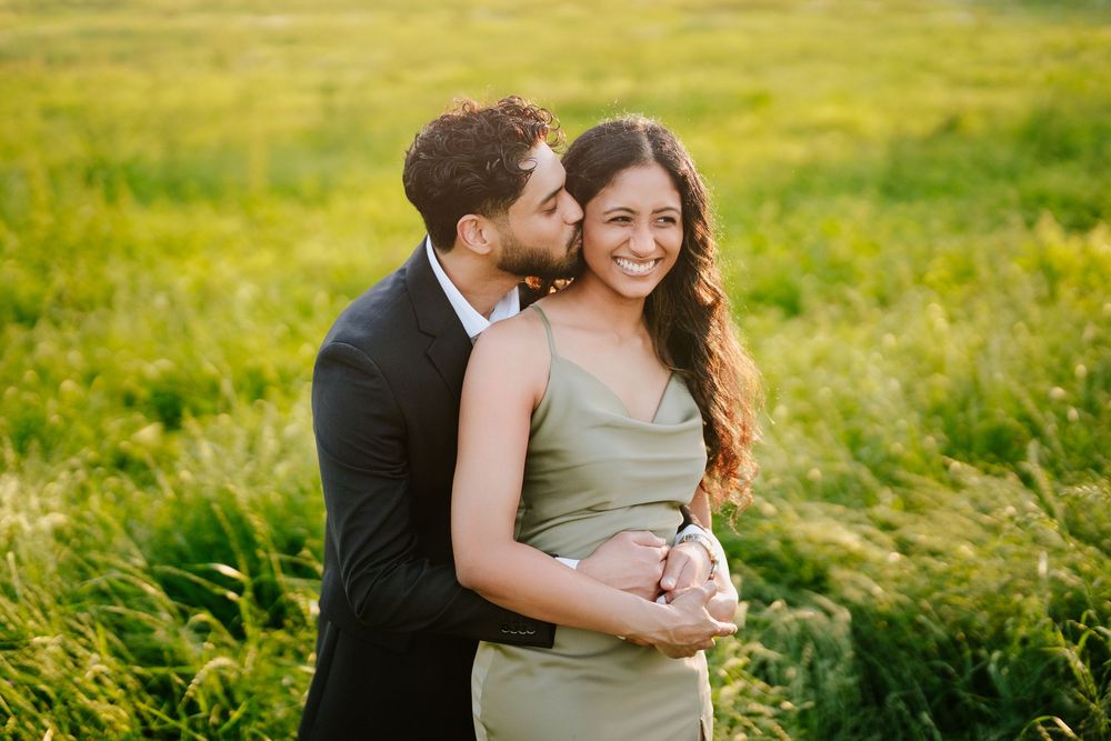 Couple shares intimate moment together while embracing in sunny meadow with golden afternoon light.