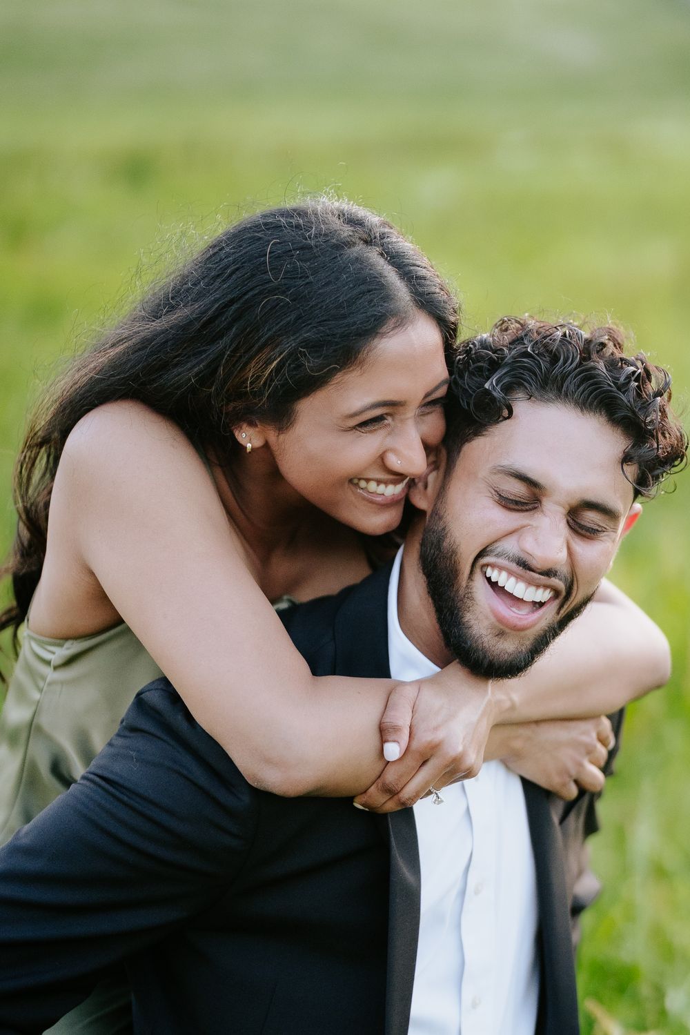 A joyful couple sharing a candid moment of laughter together in a sunny green field.