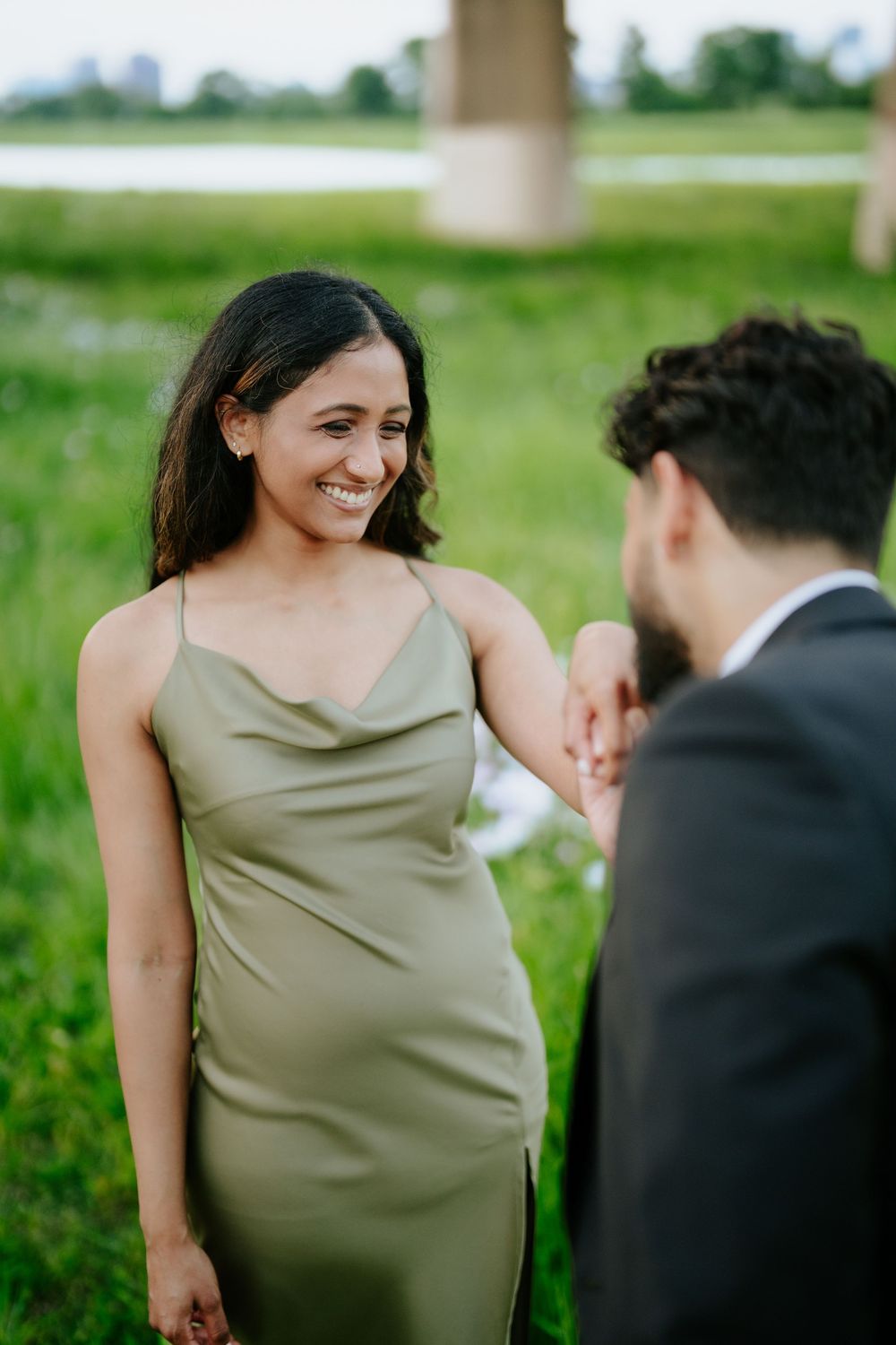 Two people share a tender moment outdoors in formal attire, with one wearing an elegant sage green dress.