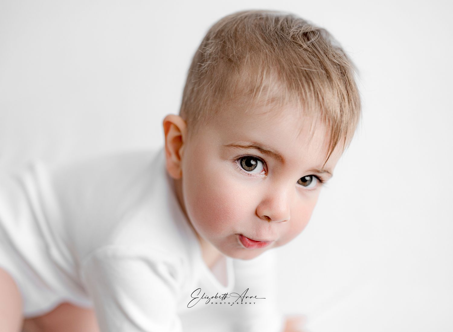 Young child in white clothing looking directly at camera with a gentle expression against light gray background.