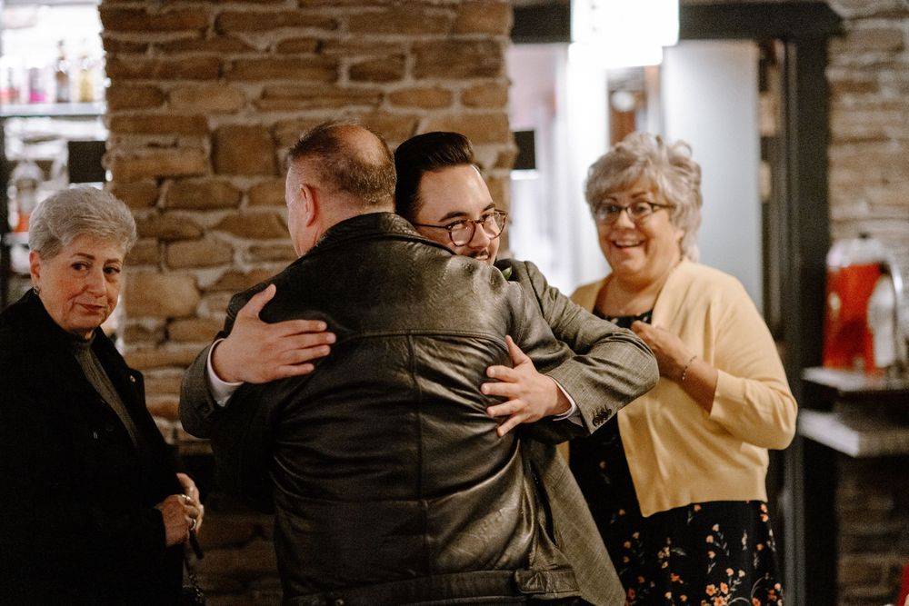 A warm embrace shared between guests at a gathering in a rustic brick-walled venue.