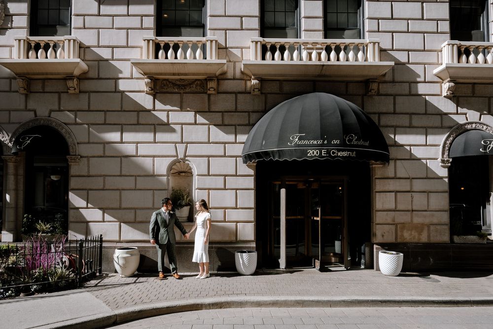 A black awning extends over the entrance of a luxury apartment building with white brick facade and ornate balconies.