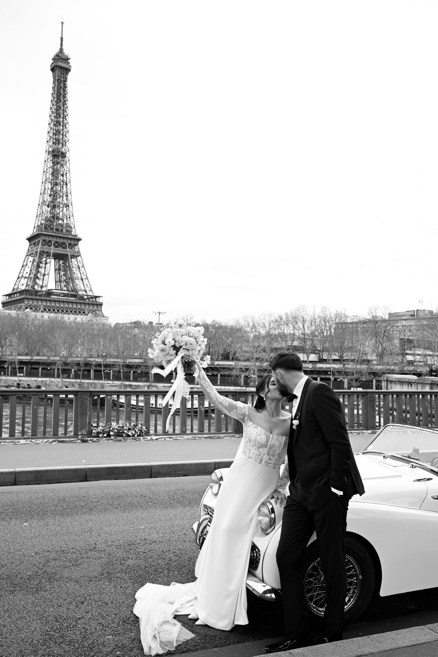 A romantic black and white embrace of a couple at a scenic overlook with cityscape and water views in the background.