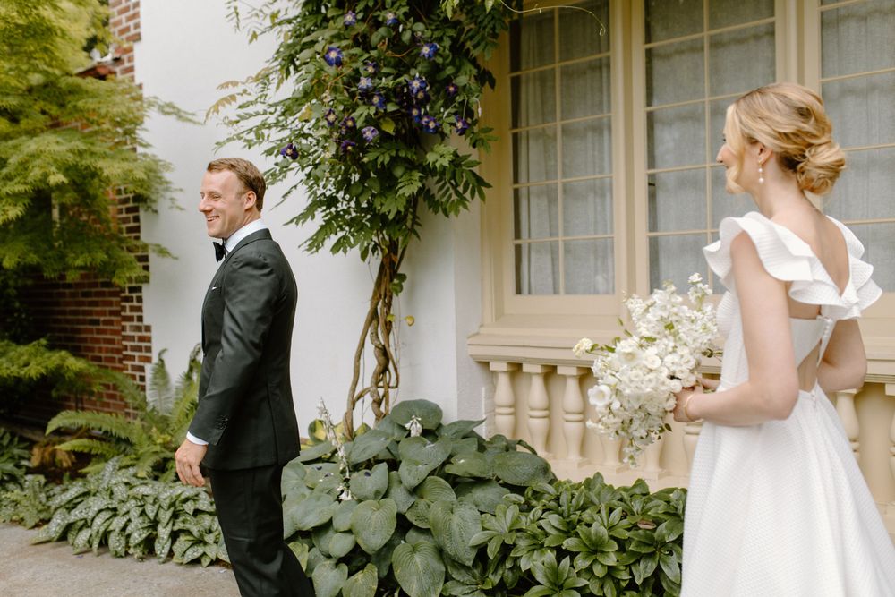 A couple sharing a first look moment before their wedding outside a white building with climbing vines.