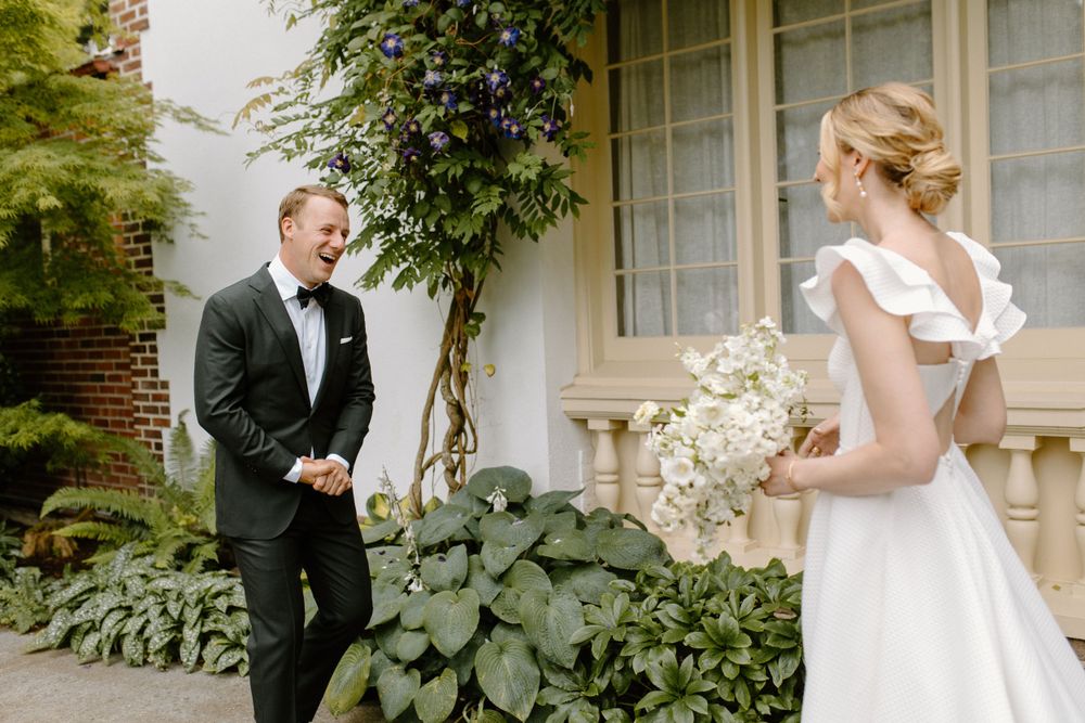 First look moment between wedding couple with groom in black tuxedo and bride in white dress with floral bouquet.