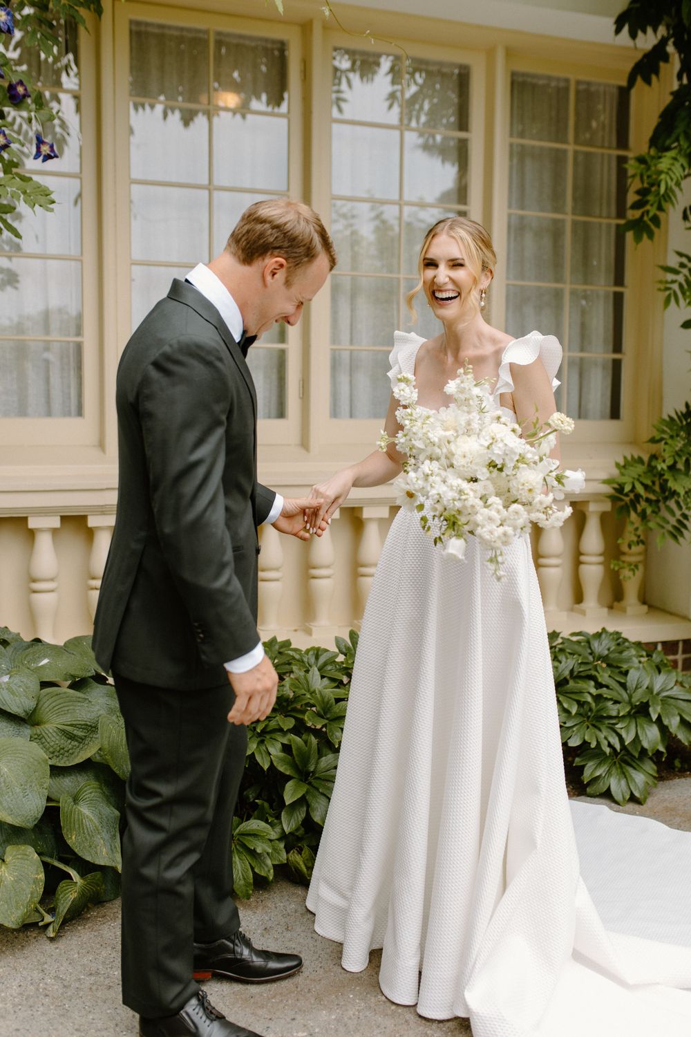 A joyful wedding moment captured outdoors with bride in flowing white gown holding elegant white florals.