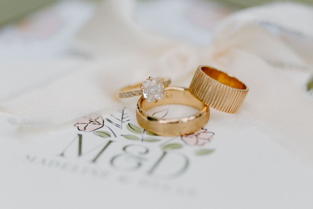 Two golden wedding rings and an engagement ring with a diamond solitaire rest on a printed paper with text.