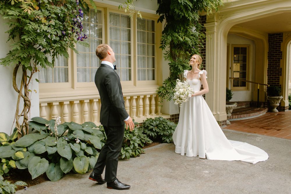 First look wedding moment captured in an elegant stone courtyard with ivy covered walls and classic architectural details.