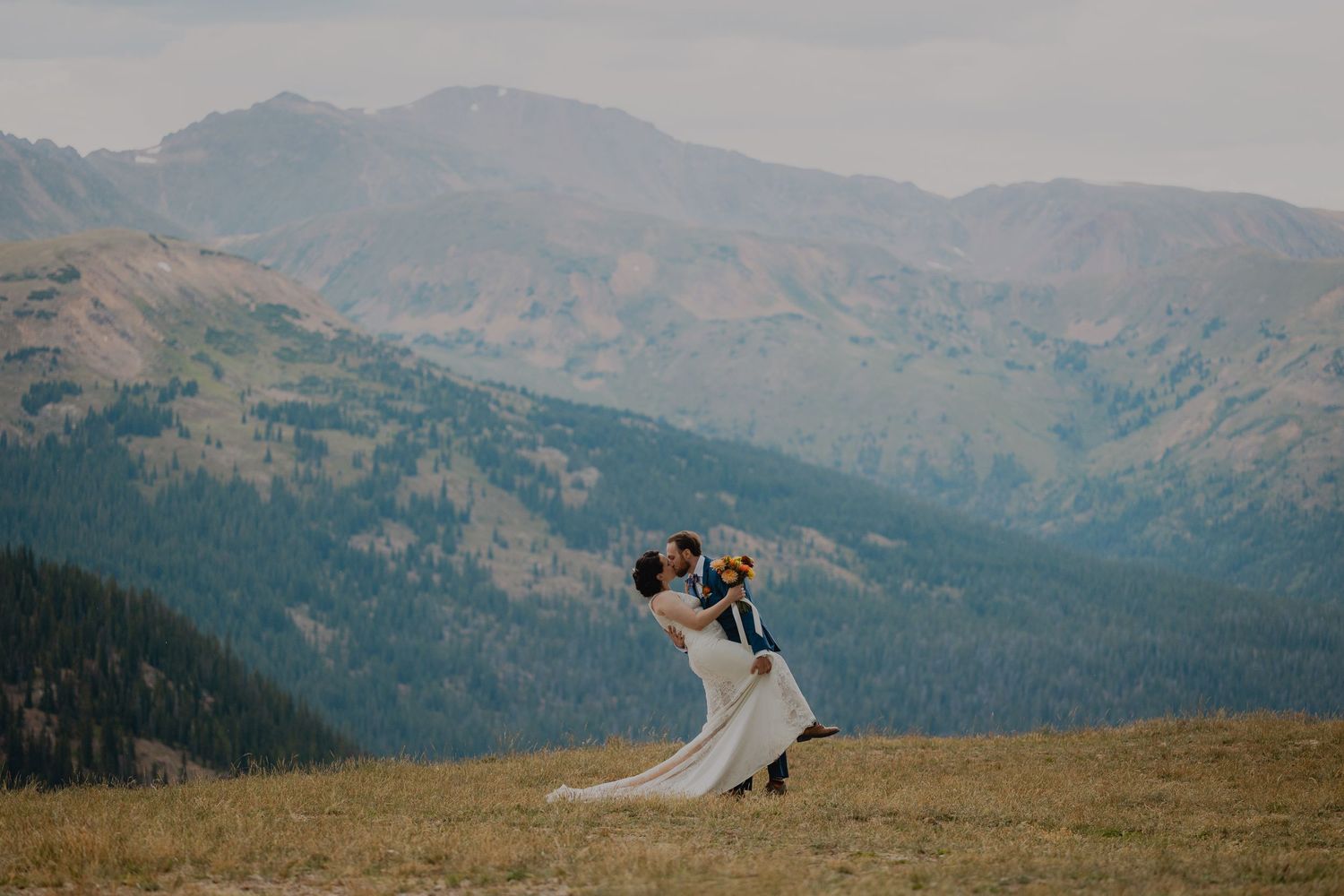 Couple dancing together on a mountaintop meadow with majestic mountain peaks and forests in the background.