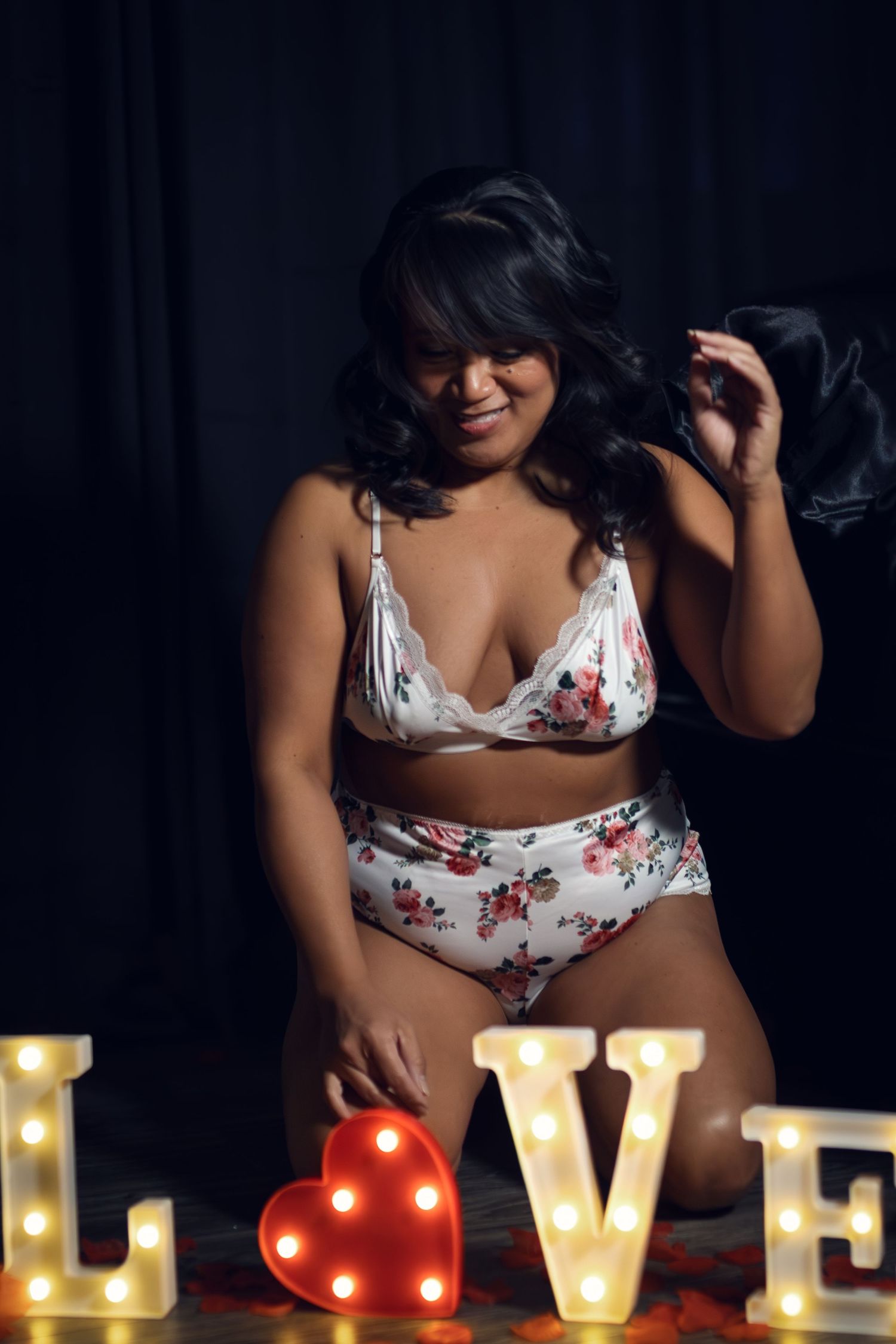 A woman in cute pjs poses with illuminated LOVE marquee letters against dark background during an empowering boudoir session in Fort Worth.