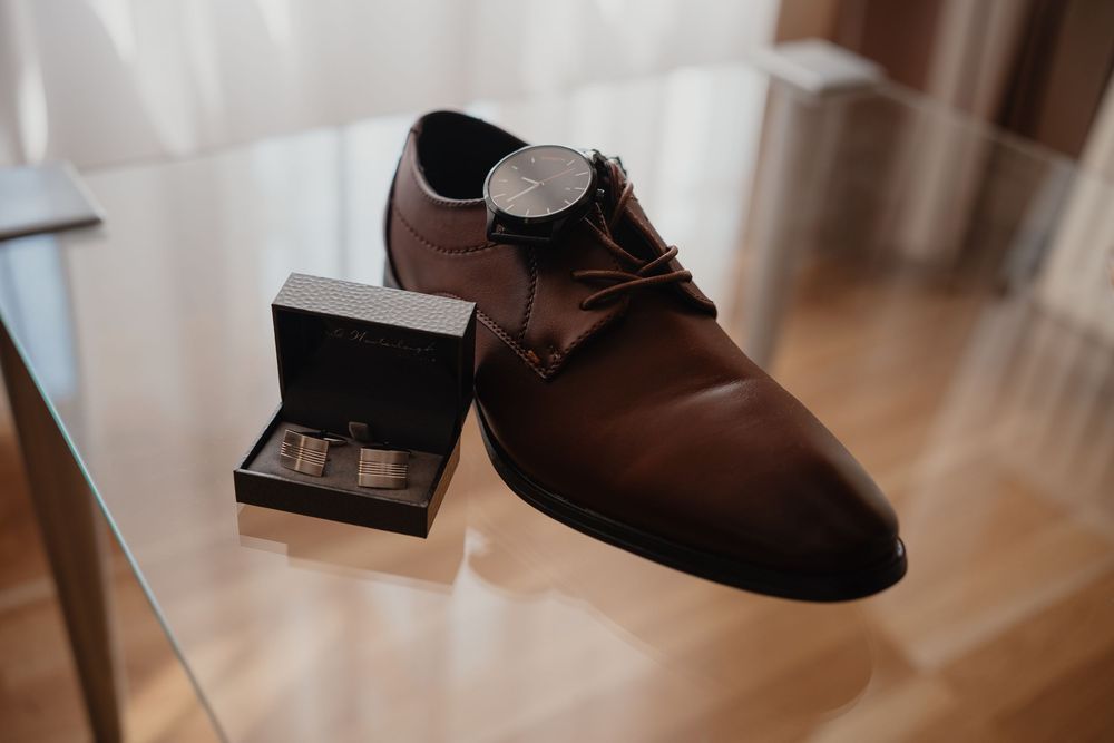 A brown leather dress shoe sits next to a black gift box on a reflective glass surface.